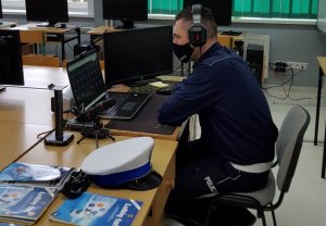 Na zdjęciu policjant Wydziału Ruchu Drogowego ze słuchawkami na uszach siedzący przed laptopem