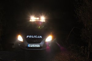 Zdjęcie przedstawiające radiowóz policyjny z włączonymi sygnałami uprzywilejowania nocą.