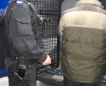 Na zdjęciu widać policjanta i zatrzymanego w kajdankach stoją obok dużego radiowozu.