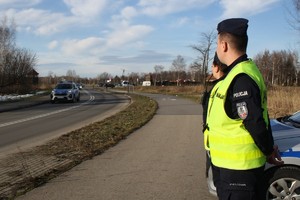 policjanci ubrani w żółte kamizelki stoją na posterunku przy ulicy obok obozu