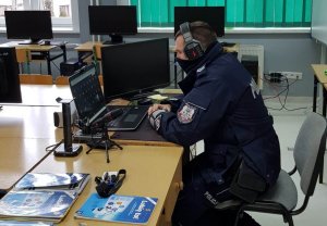 Na zdjęciu widać policjanta Prewencji siedzącego przed laptopem ze słuchawkami na uszach.