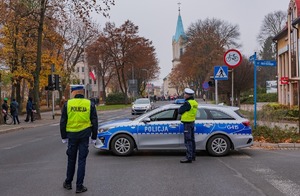 Zdjęcie  policjanci obok radiowozu na skrzyżowaniu zabezpieczają przemarsz