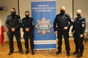Na zdjęciu dwóch policjantów i dwie policjantki. Pośrodku roll up z gwiazdą policyjną i napisem Komenda Powiatowa Policji w Oświęcimiu.