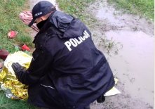 Policjant okrywa kocem termicznym osobę leżącą na ziemi.