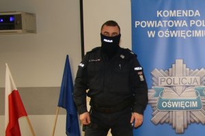 Na zdjęciu policjant w mundurze na tle roll upa z logo komendy Policji