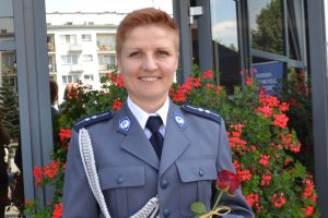 Na zdjęciu policjantka w mundurze wyjściowym na tle oszklonego budynku