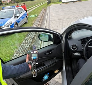 policjant z miernikiem prędkości przy samochodzie w tle radiowóz i ratownicy medyczni