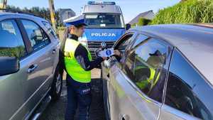 policjantka wręcza ulotkę kierowcy w tle radiowóz