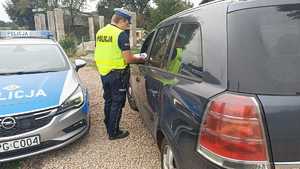 policjant wręcza ulotkę kierowcy samochodu osobowego