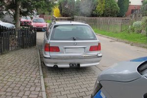 Na zdjęciu samochód bmw koloru srebrny metalik stoi na ulicy . Przed nim widać fragment radiowozu.