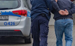 Policjant prowadzi zatrzymanego do radiowozu