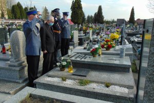 Pięć osób przy grobie. Policjanci w mundurach wyjściowych oraz przedstawiciel grupy rekonstrukcji historycznej oddają honory, przykładając dłoń do czapki.