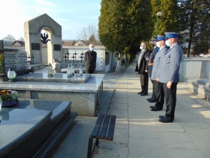 Pięć osób przy grobie. Policjanci w mundurach wyjściowych oraz przedstawiciel grupy rekonstrukcji historycznej oddają honory, przykładając dłoń do czapki.