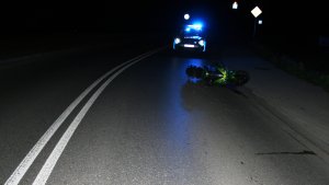 Na zdjęciu noc. Motocykl leżący na ulicy w tle radiowóz policyjny na sygnałach.