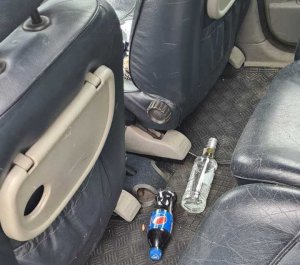 Na zdjęciu wnętrze samochodu. Za siedzeniami na podłodze szklana butelka po wódce oraz butelka plastikowa z napojem.