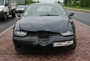 Na zdjęciu samochód marki Alfa Romeo z uszkodzonym przodem. W tle inne pojazdy.