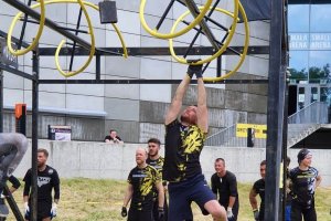 Na zdjęciu mężczyzna trzymający się metalowych rur, pokonujący przeszkodę.
Na drugim zdjęciu ośmiu policjantów w strojach sportowych z medalami w rękach. W tle szklany budynek.