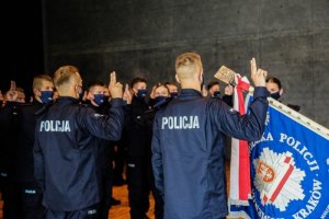 Na zdjęciu policjanci w mundurach odwróceni tyłem. Jedną rękę mają uniesioną do ślubowania