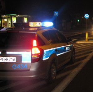 Na zdjęciu jadący nocą radiowóz z włączonymi światłami uprzywilejowania.