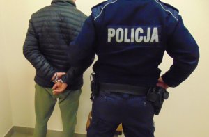 Na zdjęciu policjant z zatrzymanym stoją przy ścianie