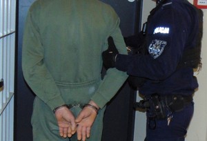 Na zdjęciu policjant i zatrzymany przed kratami