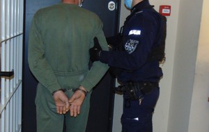 Na zdjęciu policjant oraz zatrzymany stoją przy kracie