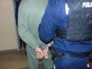 Na zdjęciu policjant z zatrzymanym. Zatrzymany ma na rękach kajdanki.