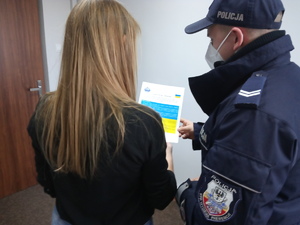Policjant  wręcza obywatelce Ukrainy ulotkę. Kobieta stoi obok policjanta.