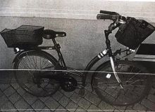 Na zdjęciu widać czarny rower z dwoma koszykami na zakupy . Jeden koszyk na kierownicy drugi na bagażniku.