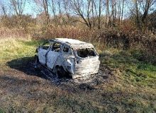 Na zdjęciu widać spalony samochód stojący przed zaroślami.