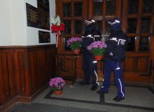 Na zdjęciu widać dwóch policjantów w mundurach składających kwiaty pod tablicą w kościele