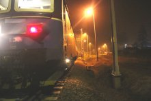 Na zdjęciu torowisko w nocy,  na którym stoi pociąg z zapalonymi światłami