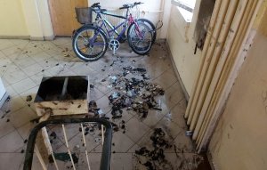 Na zdjęciu klatka schodowa ze spaloną skrzynką na podłodze w tle rowery oparte o ścianę