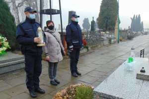 Dwóch policjant iw oraz kobieta stoją przed grobem. Policjant trzyma w ręku znicz.